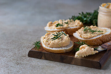 Homemade pate, spread or mousse in glass jar with sliced bread and herbs, light concrete background.