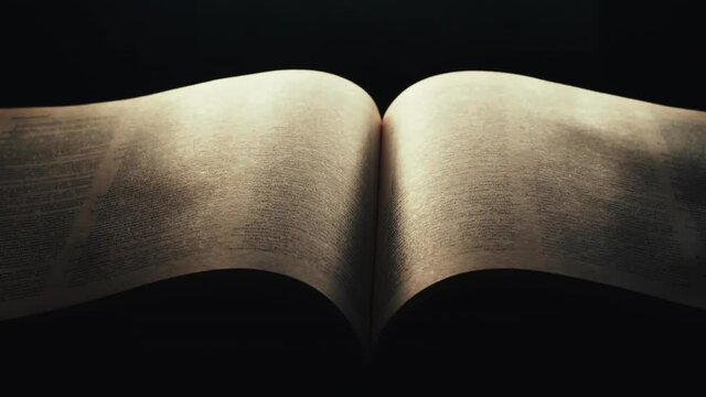 Pages gently fall open in book glowing in dark room, slow motion
