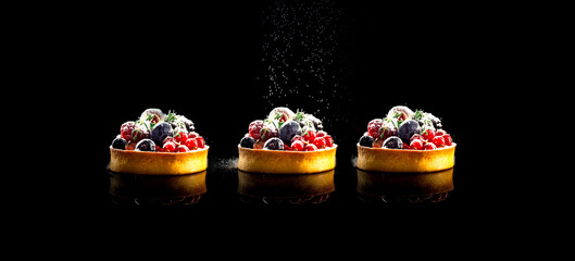 Cupcakes with berries sprinkled with icing sugar on dark background. Christmas mood or food design. Creative copy space.