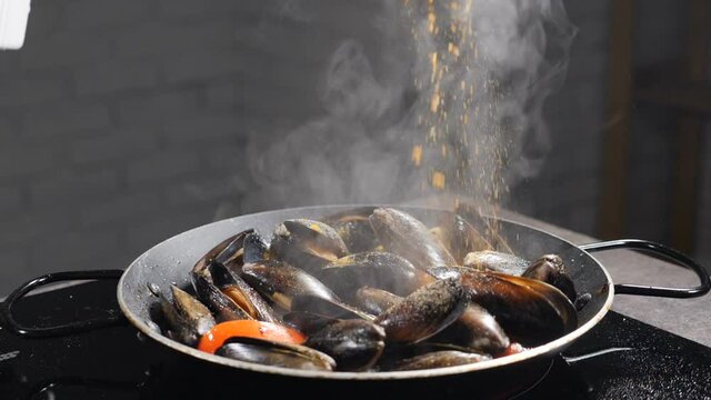 Steaming stewed mussels in white dry wine sauce with garlic and tomato. Cooking mediterranean molluscs in shell for Italian pasta. Chef adding spices and herbs. Slow motion. Full hd