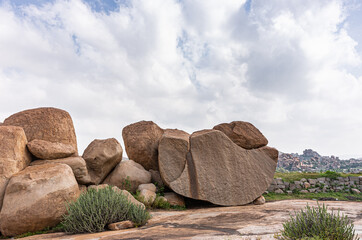 Hampi, Karnataka, India - November 4, 2013: Virupaksha Temple complex. Huge brown boulders, one cut in half, above said temple under blue cloudscape and with some green vegetation.