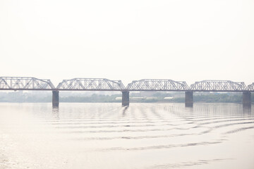 Obraz premium railroad bridge over a wide river and the silhouette of a distant city behind it in the morning fog