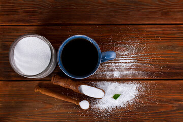 Blue ceramic cup, glass jar with wooden scoops of sorbitol and fructose on a wooden background. Different sweeteners concept. Top view.