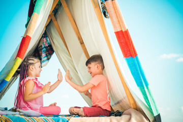 Cute lovely children play in tent. Kids playing with a teepee tent.