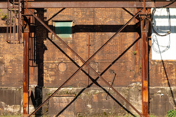 Industrial building exterior, orange brick behind heavy metal structure with rusty patina,...