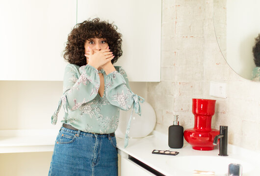 young pretty woman covering mouth with hands with a shocked, surprised expression, keeping a secret or saying oops