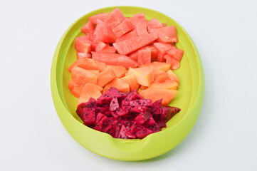 Side view of watermelons, papayas and dragon fruits assortment on a green plate.  Tropical fruits on a white background. 