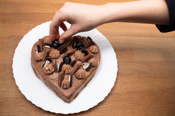 Woman decorates  heart-shaped cake base on a white plate. Wooden background.Selective focus.