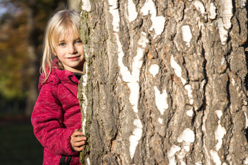 Kleines M&auml;dchen schaut unsicher hinter Baumstamm hervor