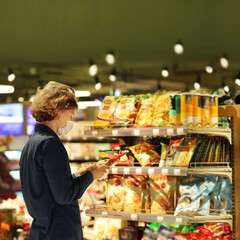 Supermarket shopping, face mask and gloves,Young man shopping in supermarket, reading product information.