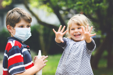 Fototapeta premium School kid boy helping little toddler sister cleaning hands with sanitizer spray. Brother and cute little girl learn hygiene rules. Family during coronavirus and flu lockdown. Covid virus protection.