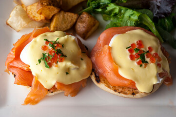Eggs Benedict is Breakfast or brunch favorite: English muffin with poached eggs, ham, lox, spinach, cheese and hollandaise sauce. Served with potato hash. Classic French bistro entree.