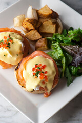 Eggs Benedict is Breakfast or brunch favorite: English muffin with poached eggs, ham, lox, spinach, cheese and Hollandaise sauce. Served with potato hash. Classic French bistro entree.