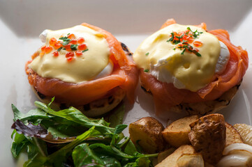 Eggs Benedict is Breakfast or brunch favorite: English muffin with poached eggs, ham, lox, spinach, cheese and Hollandaise sauce. Served with potato hash. Classic French bistro entree.