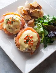 Eggs Benedict is Breakfast or brunch favorite: English muffin with poached eggs, ham, lox, spinach, cheese and Hollandaise sauce. Served with potato hash. Classic French bistro entree.