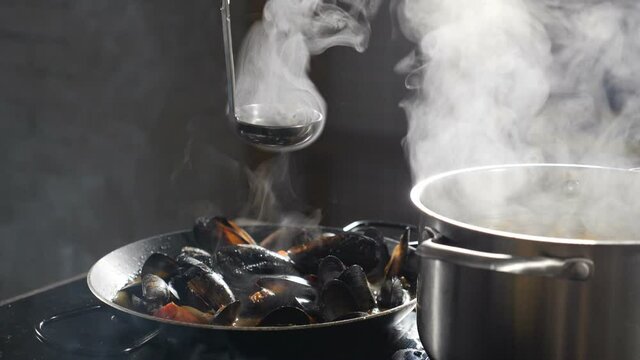 Cooking delicious seafood pasta with mussels in frying pan. Shot in slow motion. Broth being poured out of ladle.Steam rising up. Traditional Italian cuisine. Cooking in restaurant. Full hd