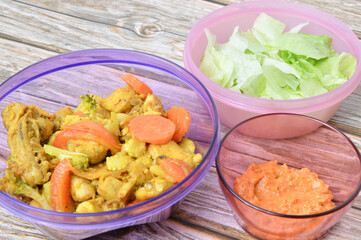 Selective focus of turmeric chicken with carrots, salads, and spicy fermented durian or sambal tempoyak in a purple bowl over wooden background