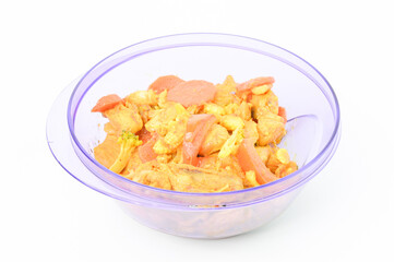 Side view of turmeric chicken with carrots, tomatoes and corns in a purple bowl over wooden background. 