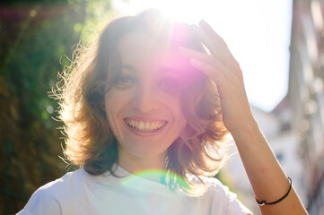 Female portrait of beautiful student, pretty girl with short hair in white t-shirt spending time outdoors near old stone wall during sunny spring or summer day