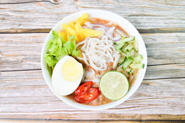 Top view of Noddle in Tangy Fish Gravy or Laksa Utara is a Special Malaysian Food Popular in Penang served with egg, lime, cucumber, chilies, pineapples and salads.