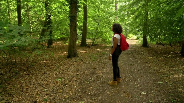 Teenage African American mixed race  girl young woman hiking with red backpack and taking photographs with a mobile smart cell phone in forest woodland 
