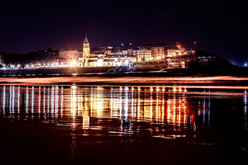 Fototapeta na wymiar Gijón,Asturias España, Playa de San Lorenzo de noche con la Iglesia de San Pedro reflejada en el mar.
