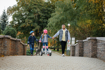 A father helps and teaches his young children to ride a Segway in the Park during sunset. Family vacation in the Park.