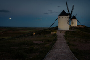 Exterior view of windmills in the landscape in spring at dusk with full moon in the Alcazar de San Juan, Ciudad Real, Spain