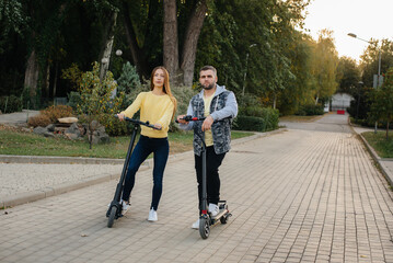 A young beautiful couple rides electric scooters in the Park on a warm autumn day. Hobbies and recreation.