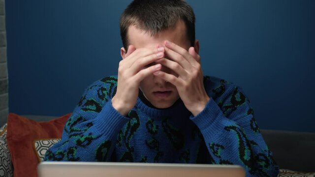 A focused tired sed young man has bed news working and using his laptop at home or office. 