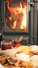 mulled wine by the fireplace, 2 glasses of drink, spices and a warm scarf by the stove