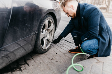 man pumps up the wheels of the car with a compressor.