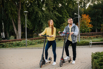 A young beautiful couple rides electric scooters in the Park on a warm autumn day. Hobbies and recreation.