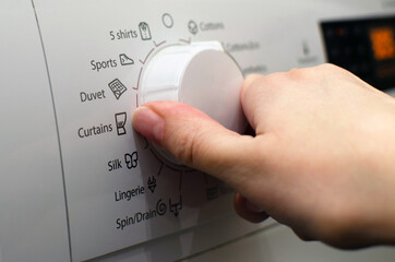 Photo of a woman setting up the washing machine, adjusting the washing parameters, turning on the washing.