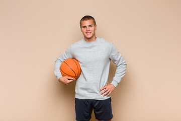 young blonde man smiling happily with a hand on hip and confident, positive, proud and friendly...