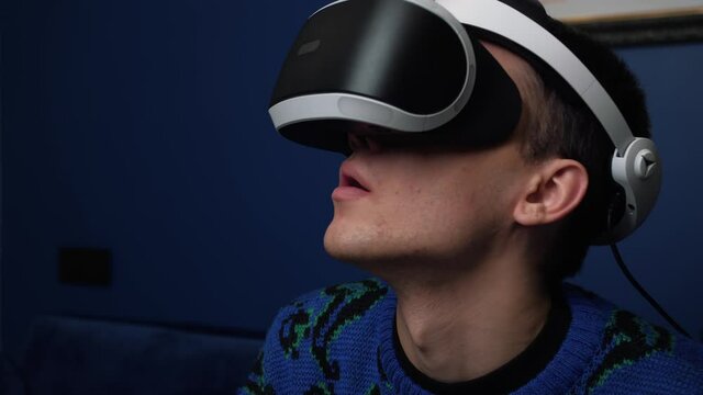 Close up Slow motion scene video of a caucasian man using a VR headset helmet device to play video games at home. 