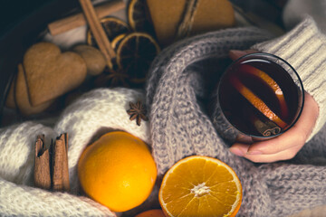 Obraz na płótnie Canvas warm drinks in cold weather, a girl with a glass of gluntwine, oranges on the table, cookies, spices and a warm scarf