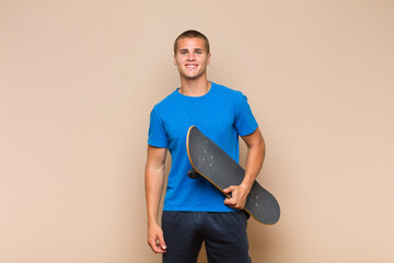 young blonde man smiling happily with a hand on hip and confident, positive, proud and friendly...