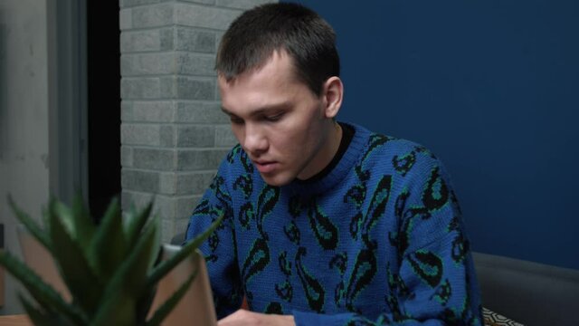 A focused tired sed young man has bed news working and using his laptop at home or office. Tired sed caucasian man uses phone.