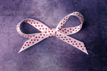 White bow with red spots over dark stone background