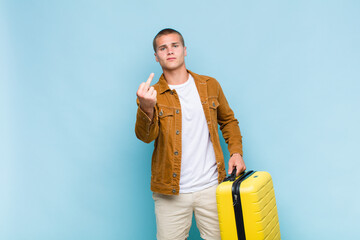 young blonde man feeling angry, annoyed, rebellious and aggressive, flipping the middle finger,...