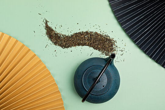 Blue Tea Pot With Dry Green Tea Leaves And Golden Paper Fan On Pastel Background. Eco Friendly Organic Brand Concept. Branding Mockup