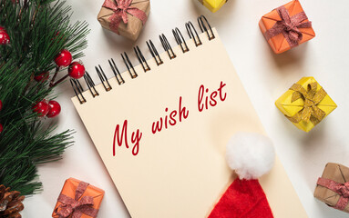 My Christmas wish list inscription on page of notebook with fir branch, wrapped gifts and red hat....