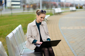 Young beautiful businesswoman with sunglasses, phone, laptop, cup of coffee in the city streets.