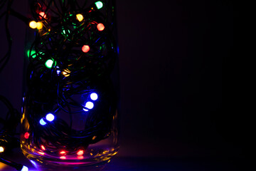 Colorful tangled christmas lights in glass on dark background with copy space.