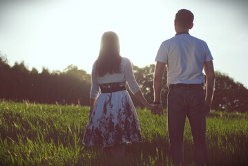 zakochani kobieta i mężczyzna spacerując , trzymając się za ręce po łące w wysokiej trawie...