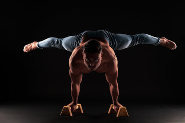 Very strong Caucasian boy doing calisthenics without a shirt with jeans doing handstand legs spread in parallel with black background
