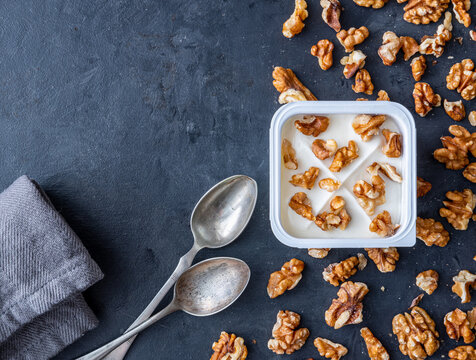 White yogurt in plastic square cup with walnuts with spoons on gray background. Flat view.