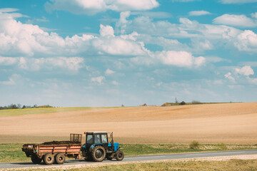 Fototapeta premium Tractor With Cart And Compost Moving On Country Road In Summer Season. Agricultural Landscape