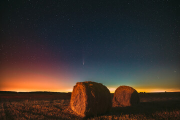 Comet Neowise C2020 F3 In Night Starry Sky Above Haystacks In Summer Agricultural Field. Night Stars Above Rural Landscape With Hay Bales After Harvest. Agricultural Concept